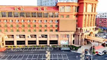 Un hotel a più piani con una facciata imponente in rosso e beige, diversi posti auto e un grande cartello con la scritta 'HUI FENG HOTEL'.