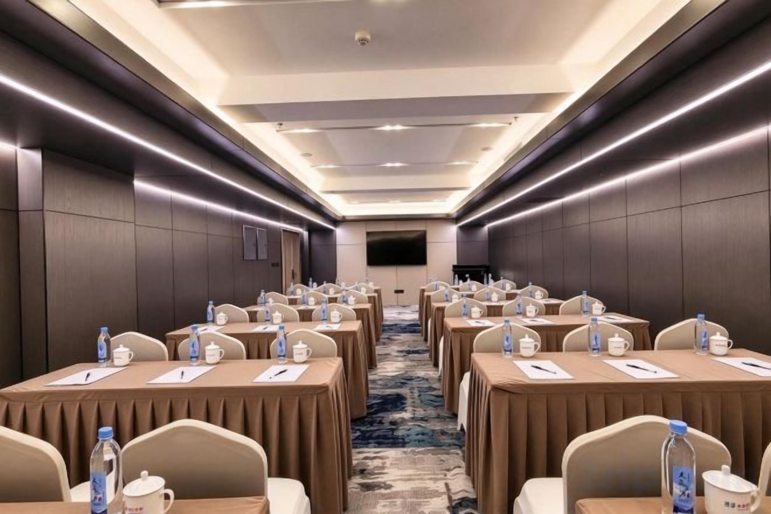 Un salón de conferencias con mesas dispuestas en filas, sillas y botellas de agua.
