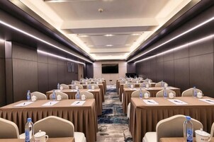 Un salón de conferencias con mesas dispuestas en filas, sillas y botellas de agua.