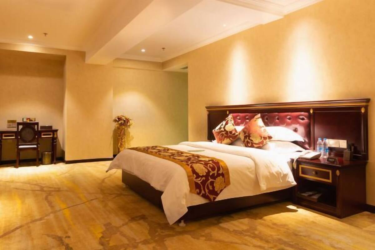 A hotel room with a large bed, a nightstand, a desk, and a vase of flowers.