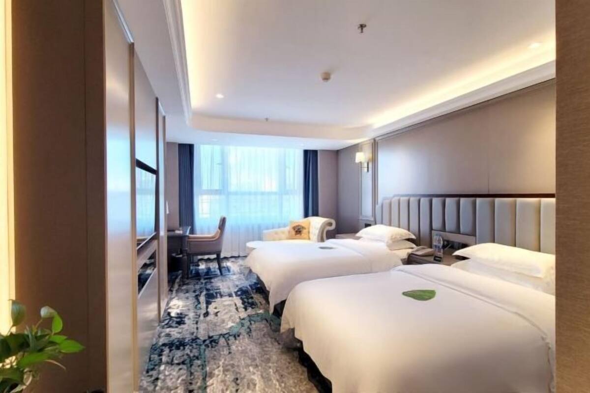 A hotel room with two beds, a sitting area with a chair, a large window, and a patterned carpet.