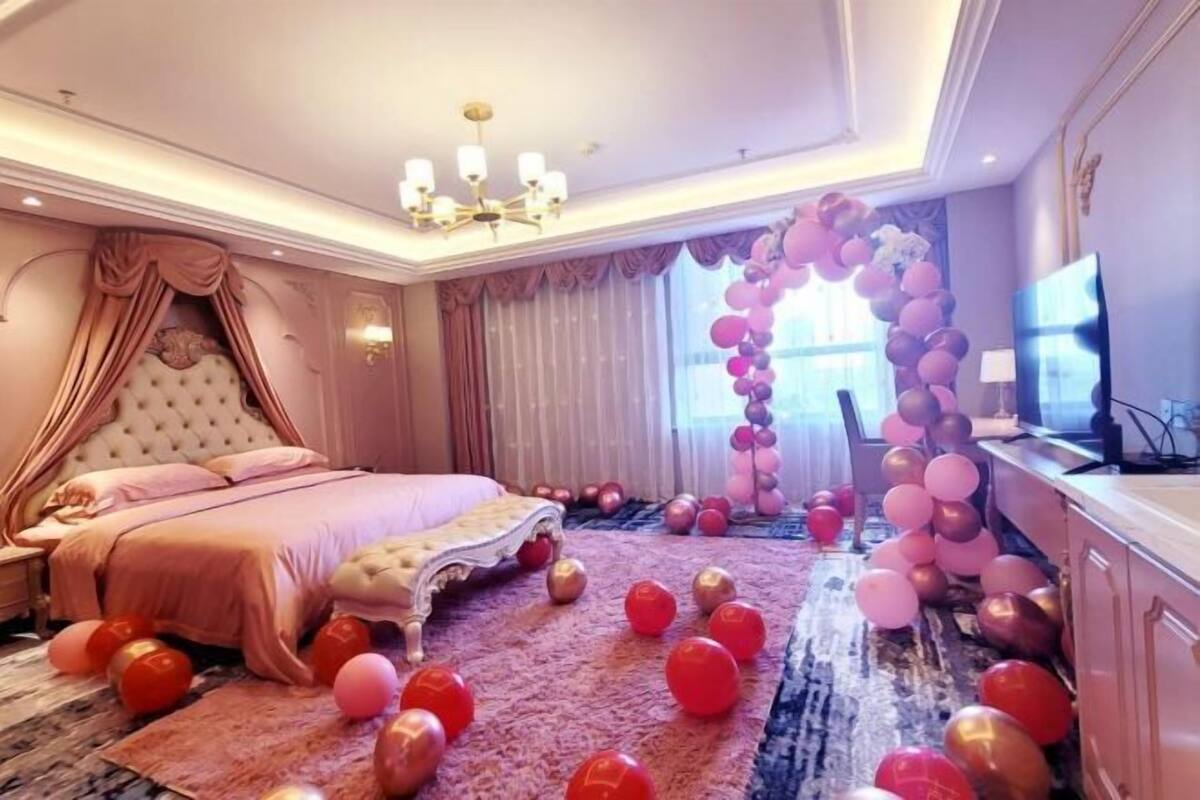 A bedroom with a large bed, a chandelier, and a wall-mounted TV.