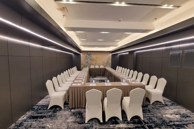 Una sala conferenze con un lungo tavolo, sedie bianche e pavimento rivestito di moquette.