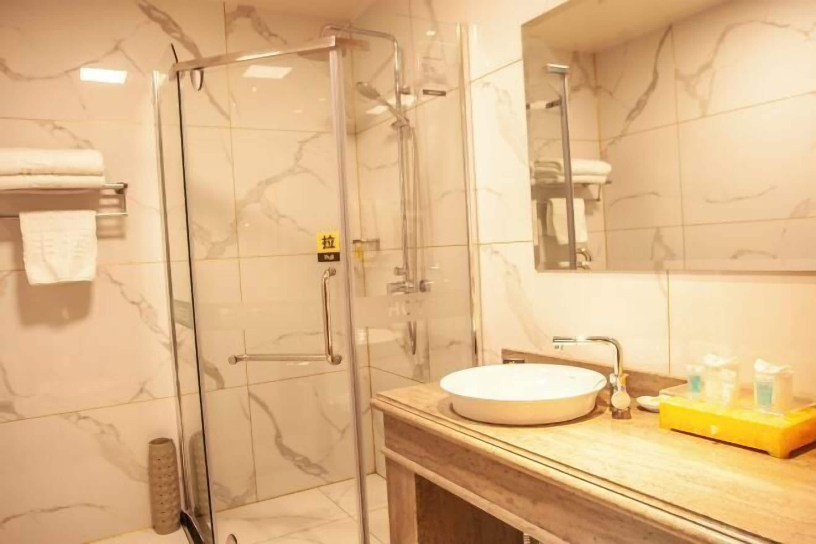 Un baño moderno con ducha envuelta en vidrio, pared con azulejos de mármol y tocador de madera con lavamanos redondo.