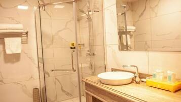 Un baño moderno con ducha envuelta en vidrio, pared con azulejos de mármol y tocador de madera con lavamanos redondo.