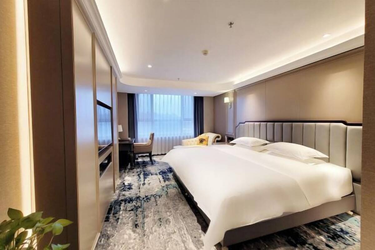 A hotel room with a large bed, a desk with a chair, a TV, and a window with curtains.