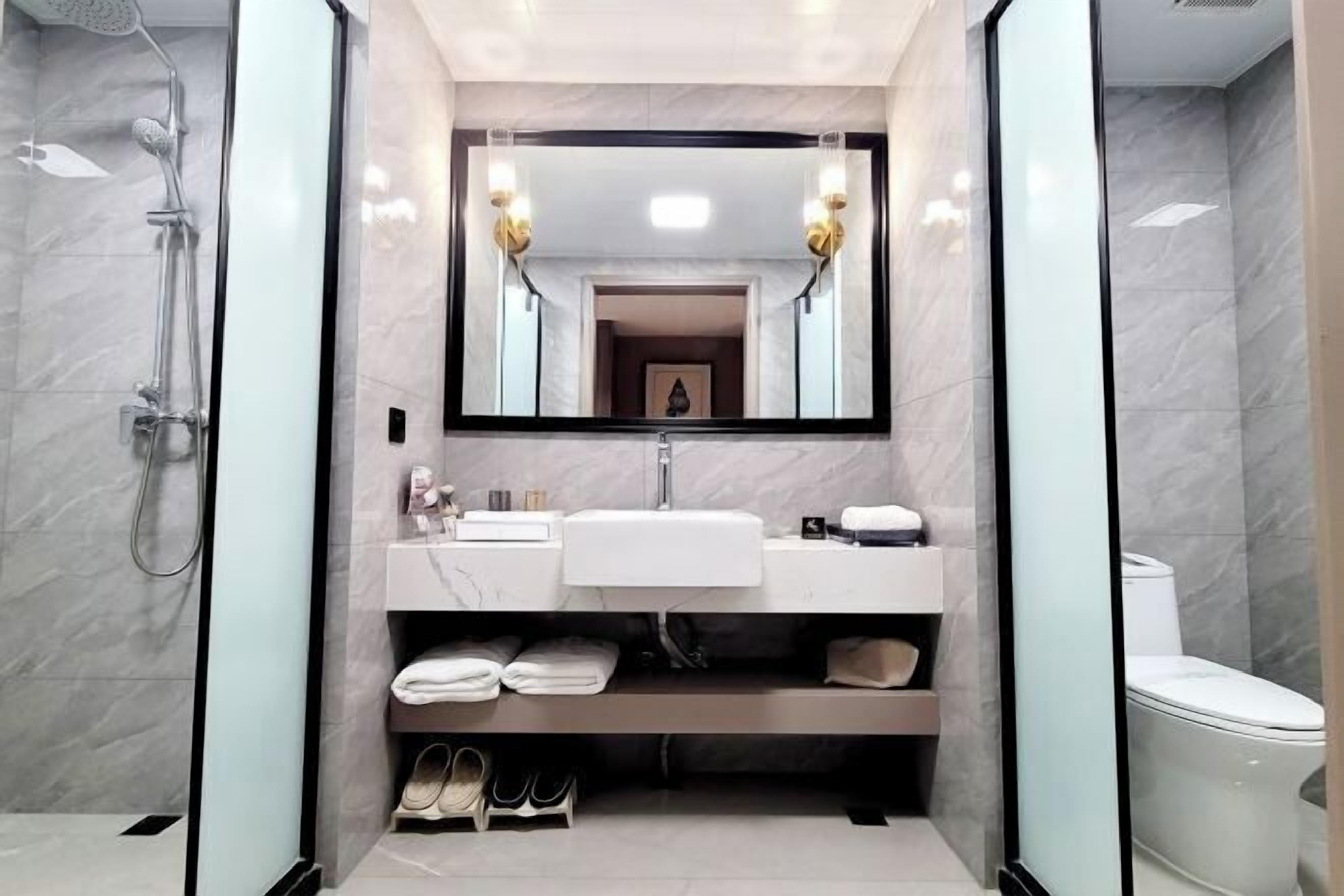 Une salle de bain moderne avec une douche à parois de verre, un lavabo blanc avec un miroir au-dessus et des toilettes.