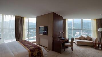A hotel room with a bed, a desk, a sofa, a TV, and large windows with a city view.