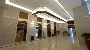Un hall d’hôtel moderne avec un sol ciré, un grand luminaire décoratif et un comptoir d’accueil.