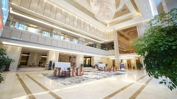 Un hall d’entrée spacieux avec un plafond haut, un grand lustre et un espace détente avec des tables et des chaises.