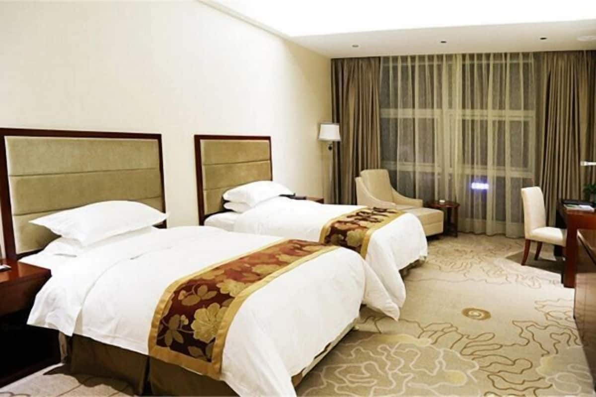 Een hotelkamer met twee bedden, een bureau, een stoel en een groot raam met gordijnen.