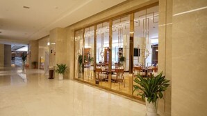 Un hall d’hôtel doté d’un sol en marbre poli, d’un comptoir de réception et d’un espace détente avec des tables et des chaises.