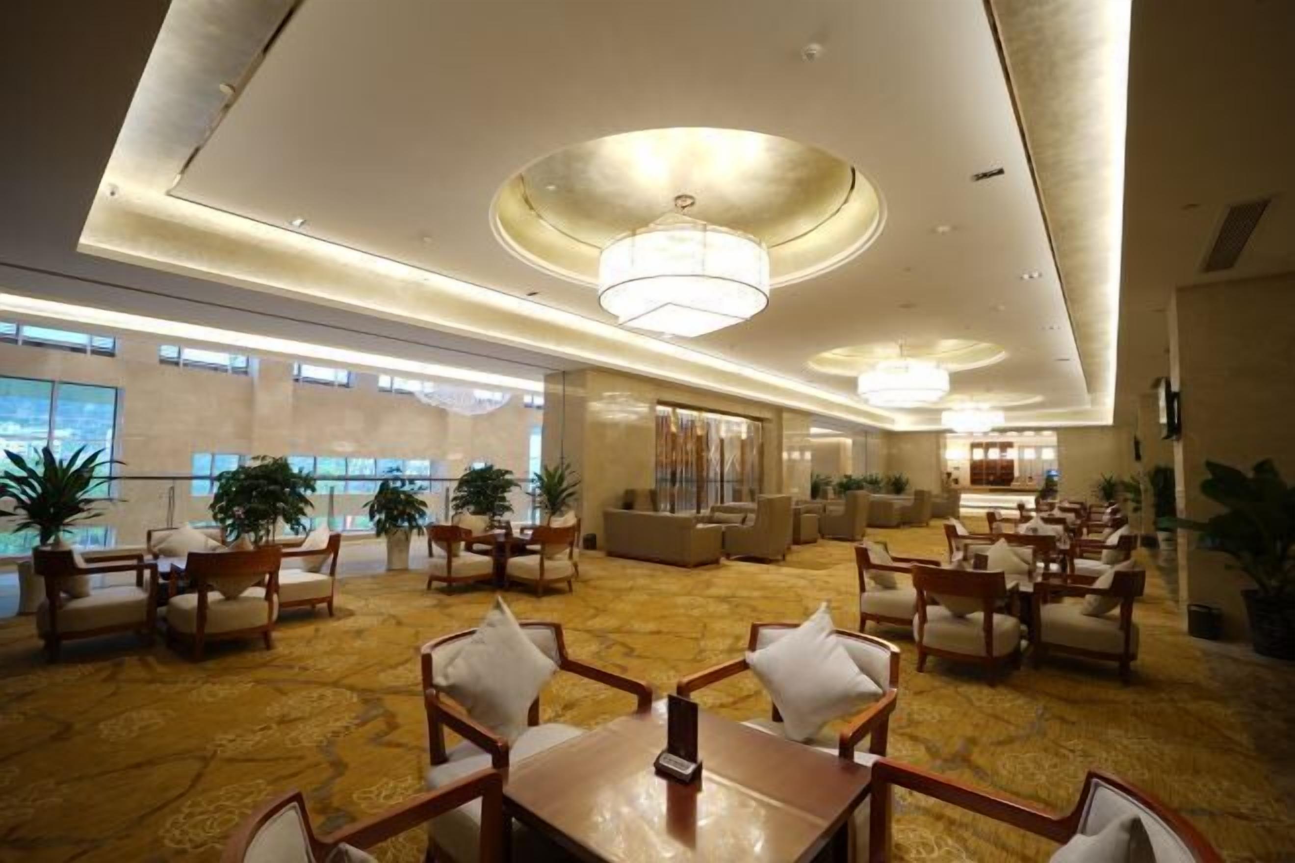 A spacious lobby with a high ceiling, chandeliers, and a carpeted floor. There are multiple seating areas with chairs and tables.