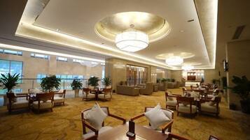 A spacious lobby with a high ceiling, chandeliers, and a carpeted floor. There are multiple seating areas with chairs and tables.