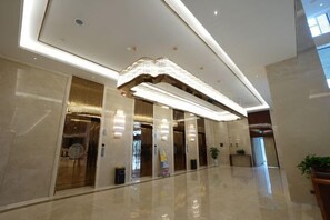 Eine moderne Hotelhalle mit glänzendem Boden, einer zentralen Leuchte und einer Rezeption.