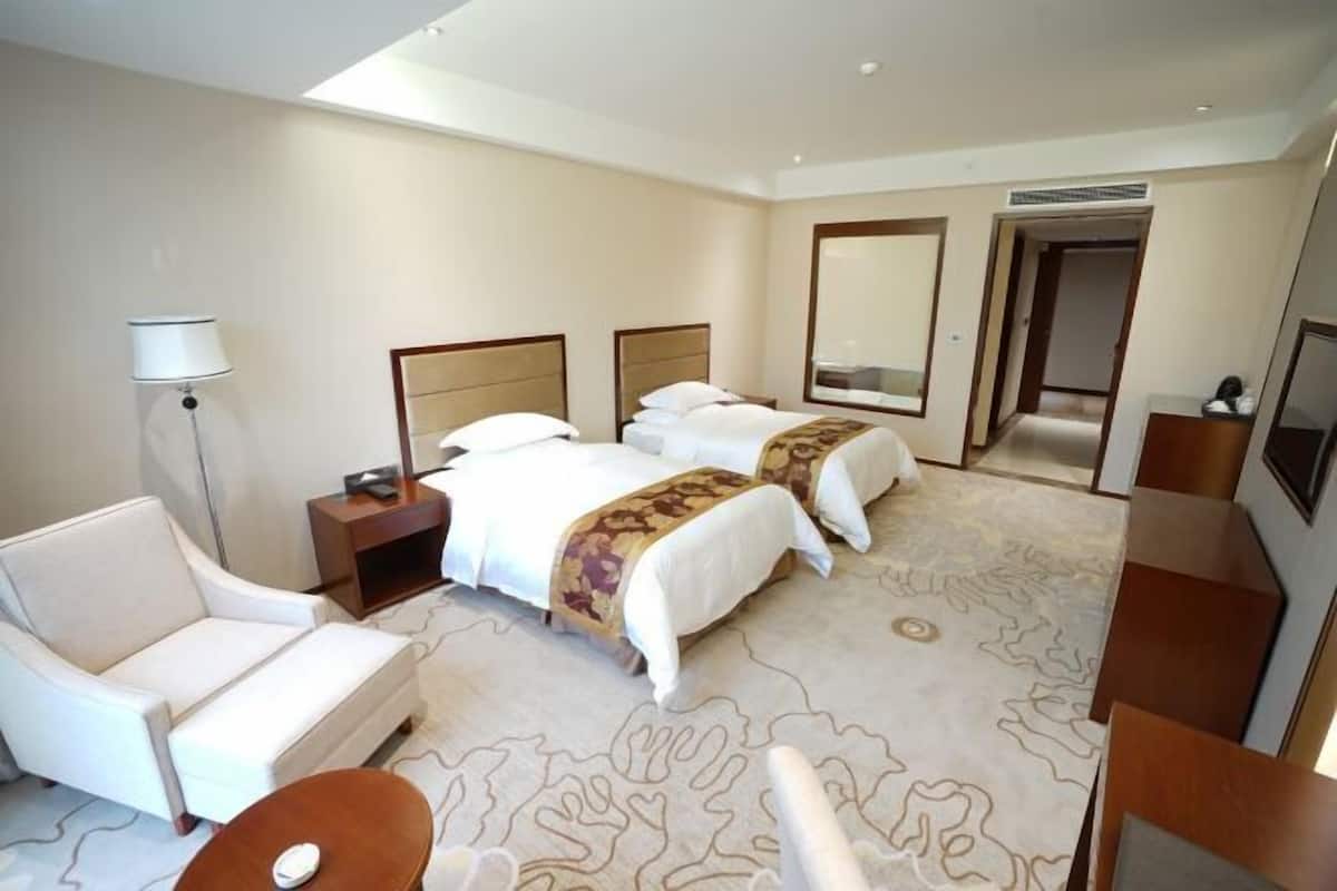 Een hotelkamer met twee bedden, een slaapbank, een bureau, een lamp en een grote spiegel.