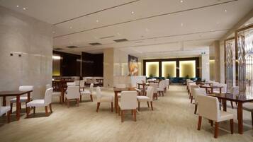 A spacious hotel dining area with multiple tables and chairs, a large window, and a modern interior design.