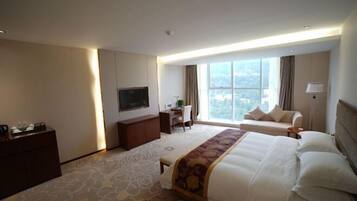 A hotel room with a large bed, a desk, a TV, and a view of the city.