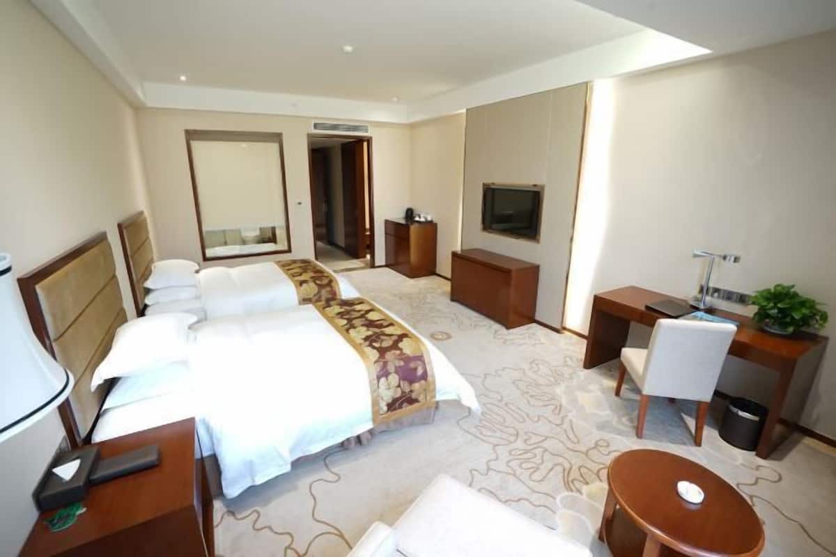 Een hotelkamer met een groot bed, een bureau, een stoel, een televisie en een bijzettafeltje.