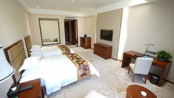 A hotel room with a large bed, a desk, a chair, a TV, and a small table.
