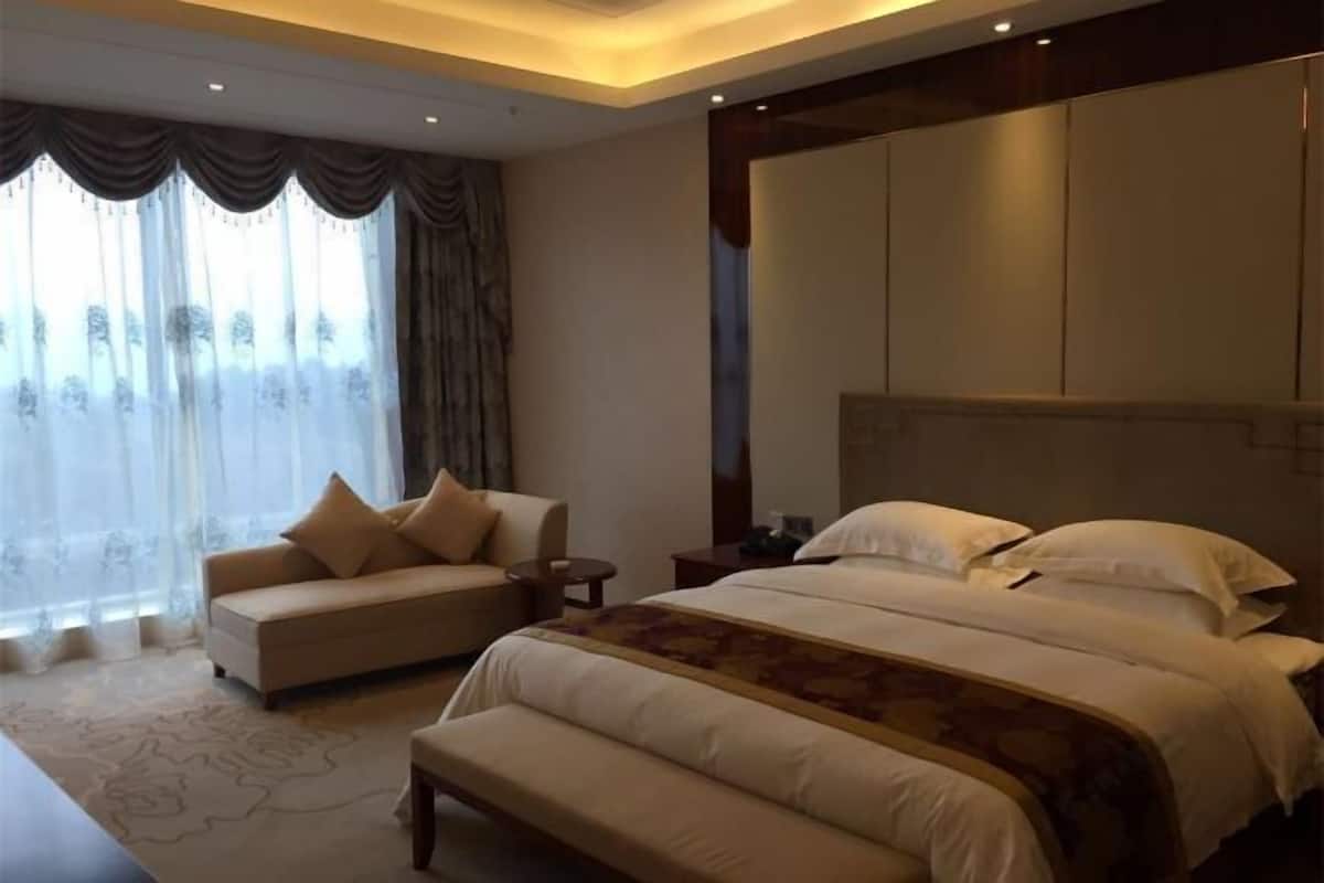 Een hotelkamer met een groot bed, een bank, een kleine tafel en een groot raam met gordijnen.