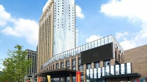 Un bâtiment moderne à la façade incurvée, doté de grandes fenêtres et bordé d’un gratte-ciel imposant.