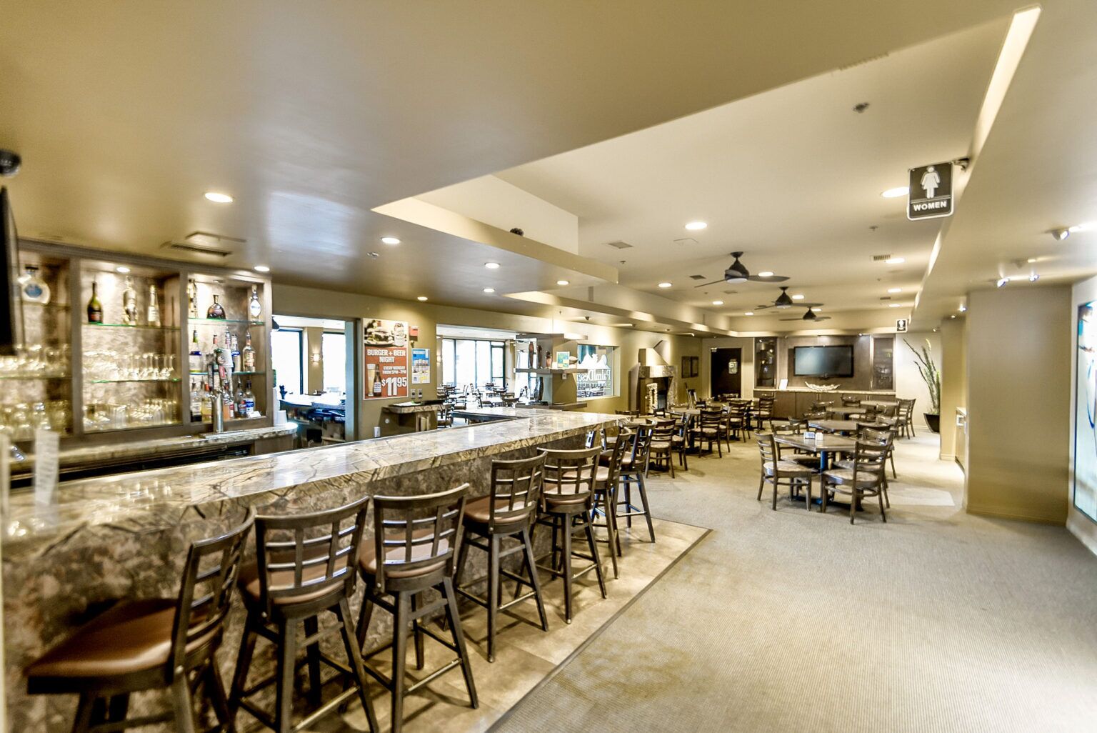 A spacious bar area with a long counter and multiple stools, a television mounted on the wall, and a clear view of the bar area.