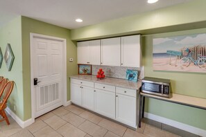 A kitchen with white cabinets, a microwave, and a beach-themed painting on the wall. - 'Sea-King Sol' Ocean-View Condo in Port Aransas! (Port Aransas)
