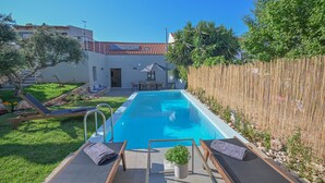 A swimming pool with lounge chairs and a small table, surrounded by a wooden fence and greenery. - Villa Garifalia with Sauna & Hydromassage (Apokoronas)