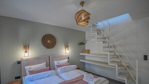 A modern bedroom with a bed, a bedside table, a wall-mounted light, a decorative wall piece, and a staircase. - Villa Garifalia with Sauna & Hydromassage (Apokoronas)
