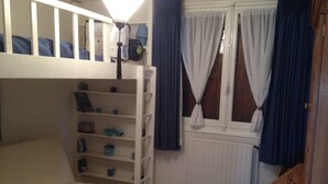 Een kamer met een stapelbed, een slaapbank, een radiator en een raam met gordijnen.