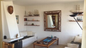 Een woonkamer met een witte bank, een houten salontafel, een boekenkast met decoratieve objecten, een grote spiegel en een klein model schip aan de muur.