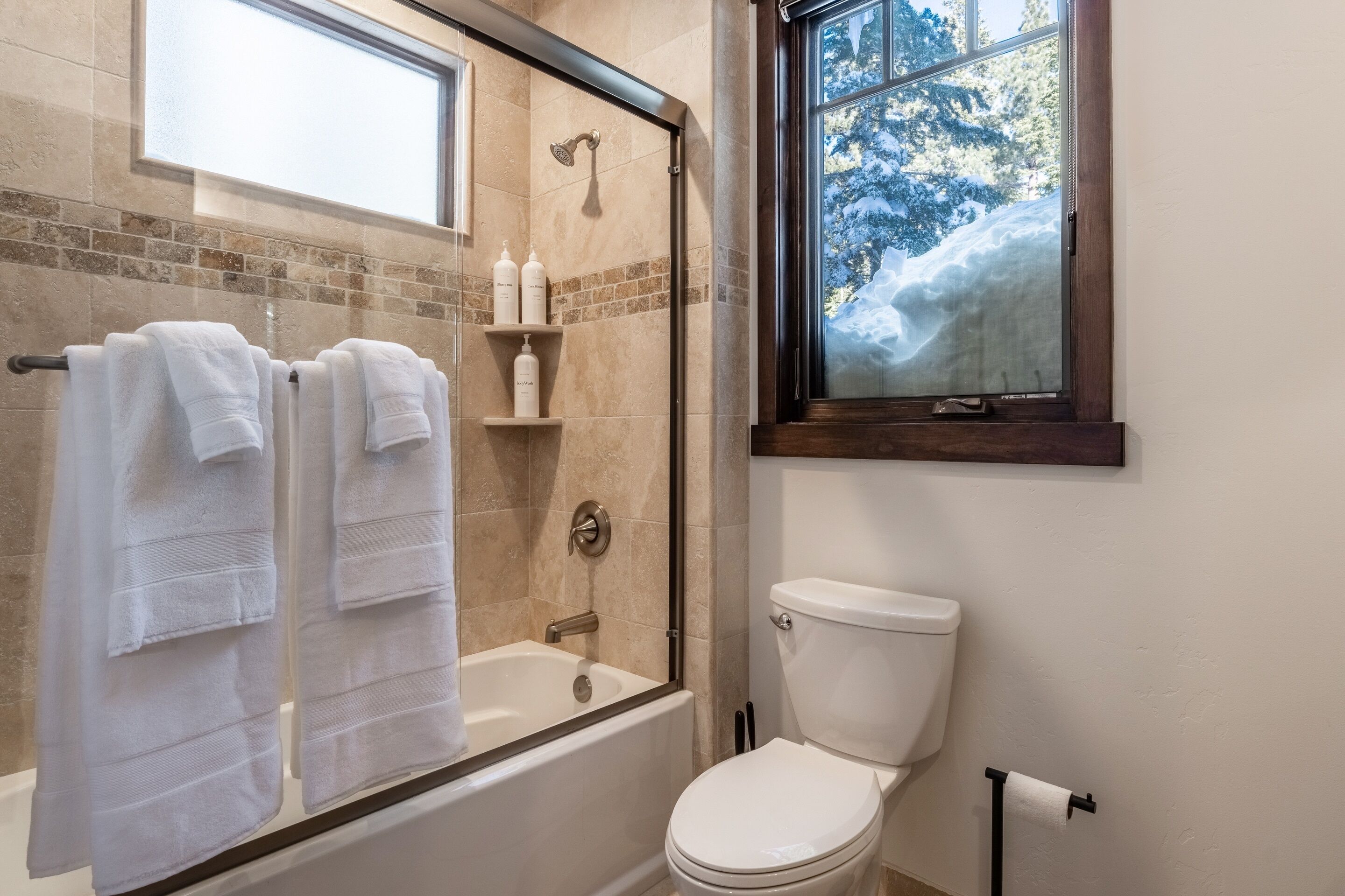 Et badeværelse med en brusekabine med glasvægge, toilet og et vindue med udsigt til træer.
