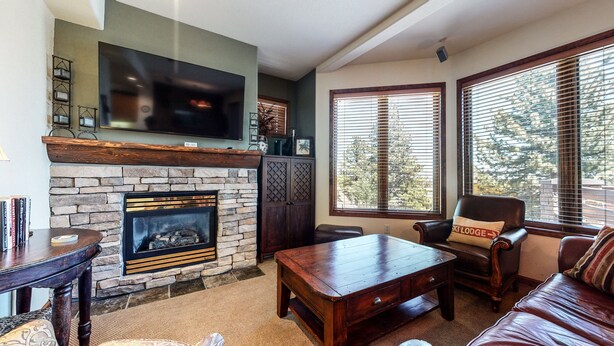 A cozy living room with a stone fireplace, leather furniture, and large windows with blinds. - Eagle Run #114 2 Bedroom Condo by RedAwning (Mammoth Lakes)