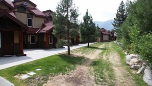 A row of modern houses with a grassy pathway between them, surrounded by trees and a mountain in the background. - Eagle Run #114 2 Bedroom Condo by RedAwning (Mammoth Lakes)