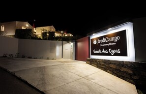 A nighttime view of a modern house with a lit signboard reading "Tradicampo EcoCountry Houses Quinta das Cycas".