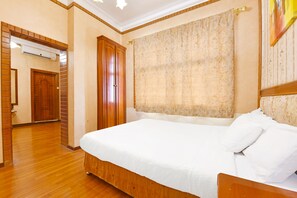 Habitación de hotel con cama de madera, un gran ventanal con cortinas, un armario de madera y una puerta que da a otra habitación.