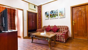 A living room with a wooden coffee table, a red patterned sofa, a television, and a wooden door. - OYO 125 Moon Plaza Hotel (Manama)