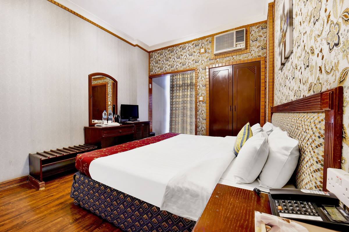 Une chambre d’hôtel avec un grand lit, un bureau avec un téléphone, un miroir et une armoire.