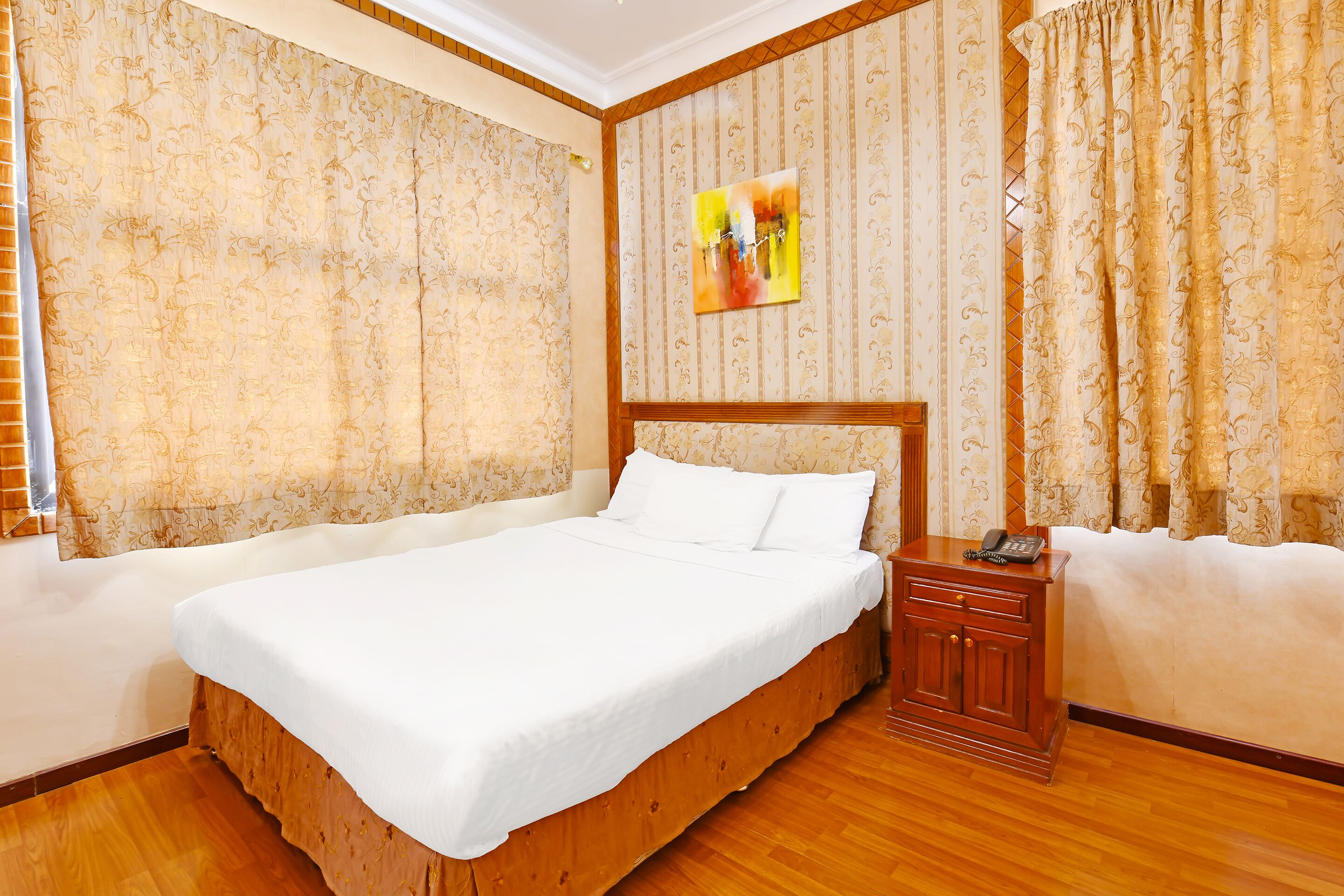 A neatly made bed with white linens, a wooden headboard, and a bedside table with a phone.