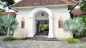 A building with a tiled roof, a stone facade, and a central archway leading to an interior space. - Omatha Village (Denpasar)