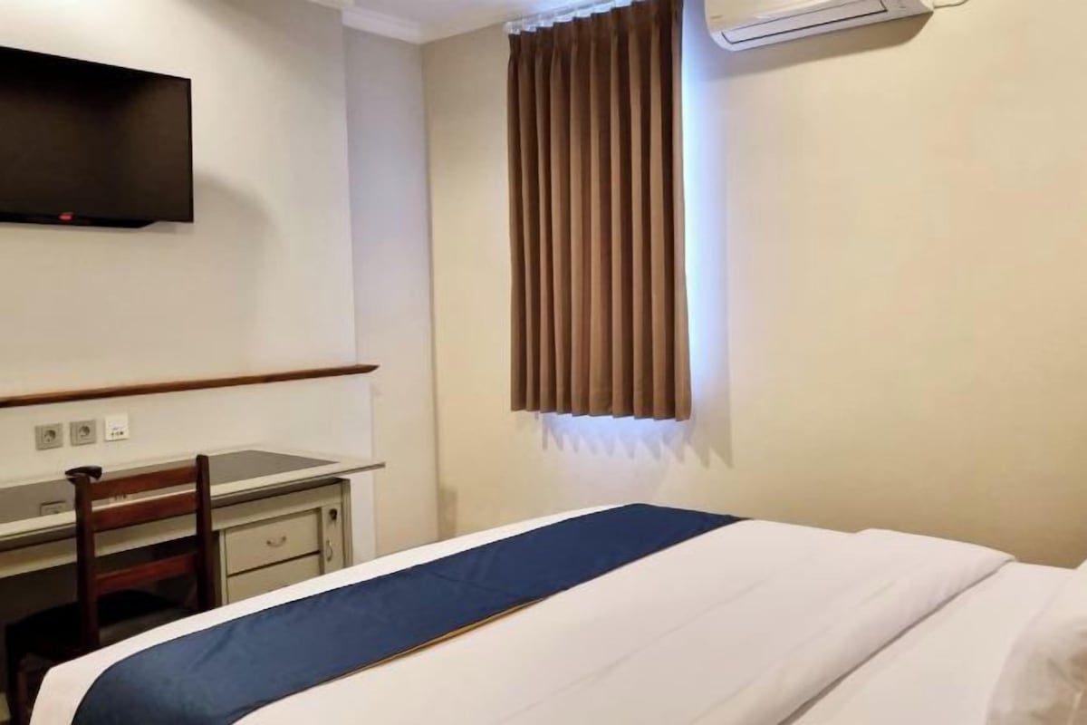 Una habitación de hotel con una cama, un escritorio y un televisor montado en la pared.