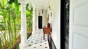 A corridor with white columns, a black and white tiled floor, and a wooden bench. - Omatha Village (Denpasar)