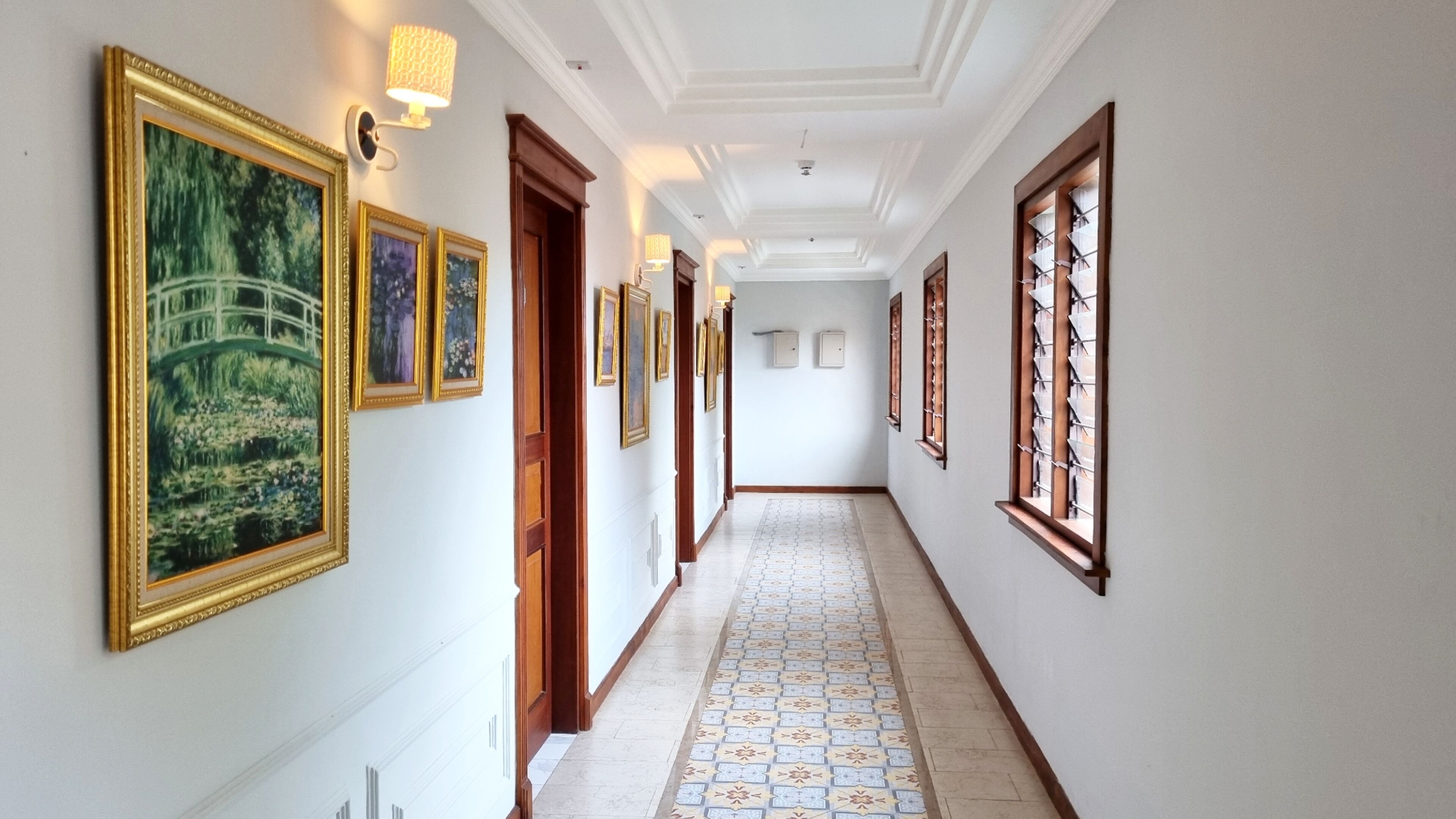 Un pasillo con baldosas de diseño, cuadros enmarcados en las paredes y puertas de madera.