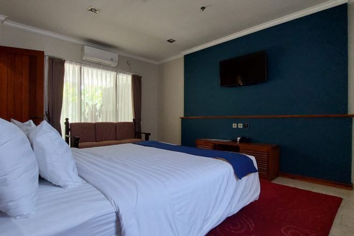 A hotel room with a large bed, a flat-screen TV mounted on the wall, and a wooden nightstand.
