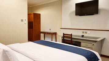 A hotel room with a bed, a desk, a chair, a TV mounted on the wall, and a wardrobe.