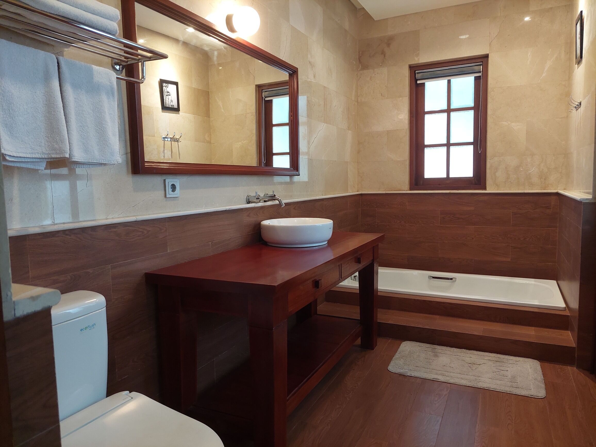 A bathroom with a wooden vanity, a white sink, a bathtub, and a toilet.
