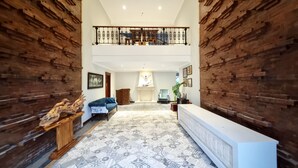 A spacious lobby with a high ceiling, a fireplace, a blue sofa, and a reception desk. - Omatha Village (Denpasar)