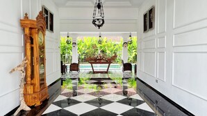 A hallway with a checkered floor, a wooden statue, and a table with a floral arrangement. - Omatha Village (Denpasar)