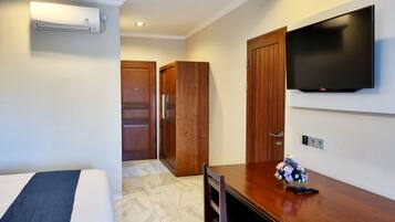 Habitación de hotel con cama, un escritorio de madera con un florero, un televisor de pantalla plana en la pared y un armario de madera.